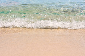 Transparent blue sea wave with white foam on a clean sandy shore, selective focus. turquoise ocean water. summer holidays border. Summertime. Empty sand beach with soft wave background. Summer rest