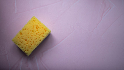 Yellow foam sponge for washing dishes and cleaning. Soft washcloths on a pink background top view.