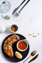 Grilled chicken breast with sauce, peanuts and lemon on a plate on stone background