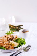 Grilled chicken breast with fresh frize salad, peanuts and lemon on a plate on stone background