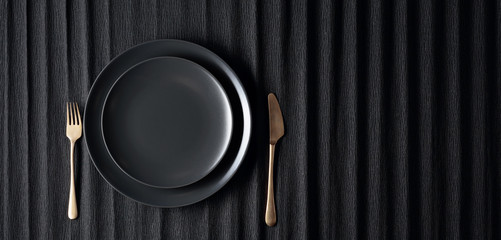 Empty black plate, fork and knife on a black background. Top view.