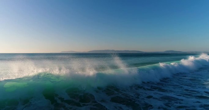Aerial view of waves breaking at the Comporta Beach with the Arrabida mountains on the background, in Portugal