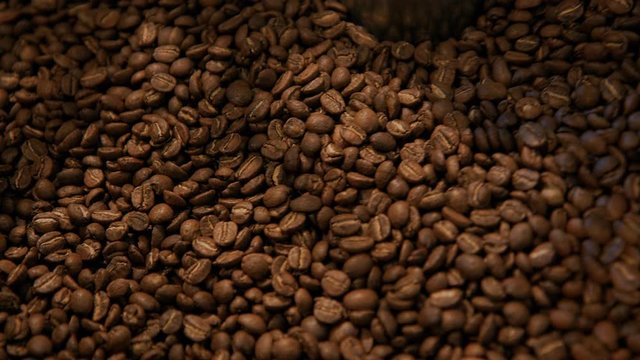 Close up slow motion cinematic beautiful shot of brown roaster coffee beans spinning and mixing in drum roaster on slow speed. Roasting proccess of small batch brewery