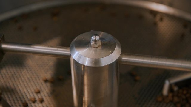 Close up of drum roaster mechanism spin in slow motion, mixing and moving coffee beans during finall proccess of roasting. Industrial beverage industry