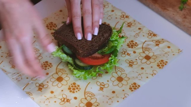 Woman hands wrapping a sandwich in beeswax food wrap