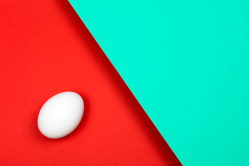 Beautiful white chicken egg on a green blue and red paper background