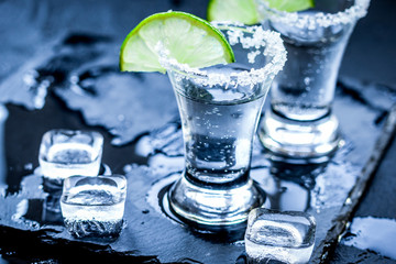 Silver tequila shots with ice and lime on black table background