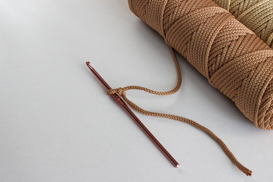 Beige crochet hook and a skein of beige cord on a white background. On one hook - a loop from the cord, made to start knitting. Such a cord can make a carpet, accessory, etc.