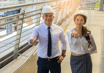 Male and female engineers inspect the site, large-scale outdoor construction projects in the modern downtown area. Engineers wear white safety helmets for safety.