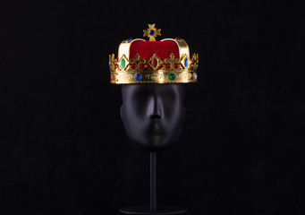 black mannequin head with crown isolated on black background