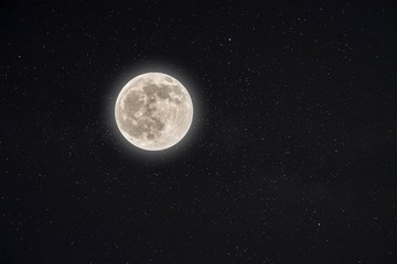 Beautiful shot of a glowing white full moon with a starry night sky in the background