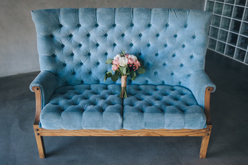 The bride’s wedding bouquet of roses and peonies lies on a blue sofa in a beautiful interior. Photography, concept.
