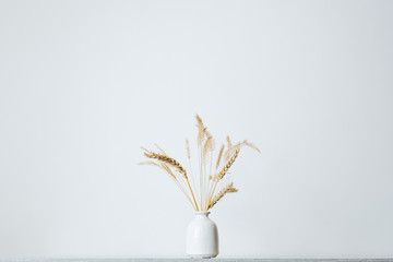 Spikelets or wheat in a vase on the table. Home decoration elements in sparse pastel background