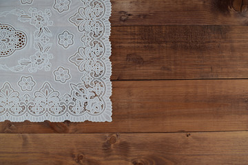 White lace napkin on brown wooden background. Vintage background with white crochet lace.