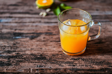 A glass of orange juice on a vintage wooden table, complemented by slices of fresh local oranges and their leaves. In Indonesia this drink is called jus jeruk.