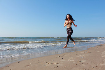 Sporty girl training outside. She is running by seaside. Athletic Fitness Woman Running on the Beach. Female Runner Jogging. Outdoor Workout. Fitness Concept.  Morning workout and sport activity
