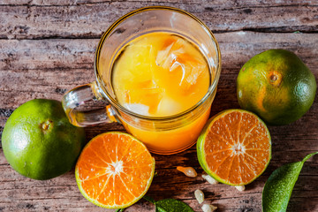 A glass of orange juice on a vintage wooden table, complemented by slices of fresh local oranges and their leaves. In Indonesia this drink is called jus jeruk.