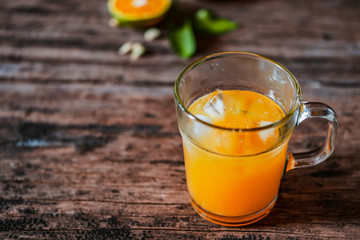 A glass of orange juice on a vintage wooden table, complemented by slices of fresh local oranges and their leaves. In Indonesia this drink is called jus jeruk.