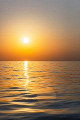 Bright sunset with large yellow sun under the sea surface. Beautiful sunset over the sea