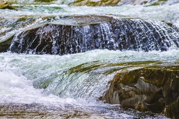 Obraz premium Stormy stream of water in a mountain river with a small waterfall_