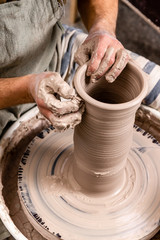 Fototapeta na wymiar Potter making a jar pot of white clay on the potter's wheel circle in studio, concept of creativity and art, vertical photo