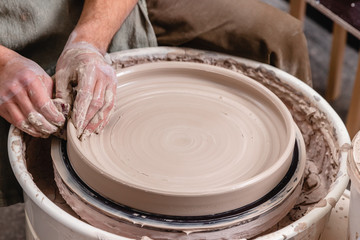 Potter making a big flat bowl of white clay on the potter's wheel circle in studio, concept of creativity and art, horizontal photo