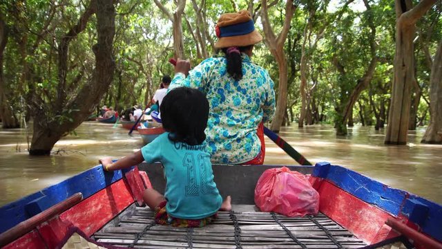Woman and kid on a raft canoe in famous flooded mangrove forest. Floating village in Tonle Sap. Popular boat trip for backpackers & tourists. 