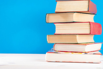 Stack of old books, blue background, free copy space. Antique old hardback books on a wooden shelf on a deck table, unmarked, empty spine. Back to school. Education