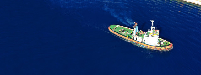 Aerial drone ultra wide photo of assisting tug boat cruising in Mediterranean logistics port with...