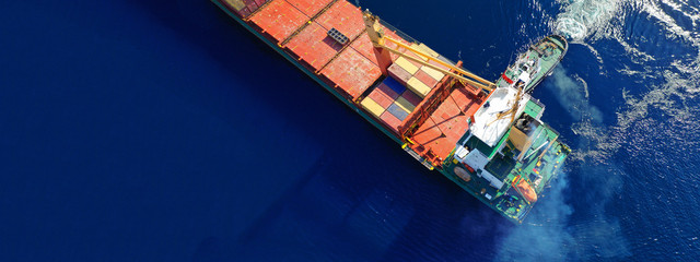 Aerial top down ultra wide photo of Container cargo Ship carrying load in truck-size colourful containers in deep blue open ocean sea 