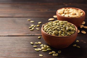 Pumpkin seeds in ceramic bowl on dark wooden background. Selective focus.