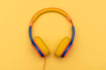 Multi-colored kids headphones on yellow pastel background. Minimalistic fashion music concept. Top view, flat lay, copy space