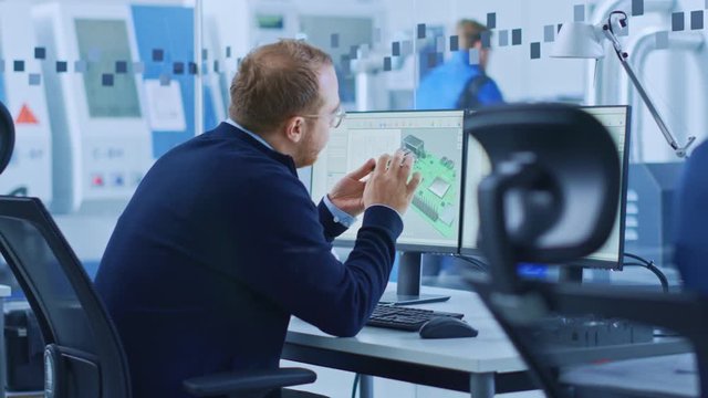 Electronics Factory: Male Electrical Engineer Holds PCB Prototype, Works on Computer, uses CAD Software to Develop Microchips, Semiconductor and Telecommunications Equipment. Manufacturing Facility