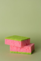 Two pink sponges for washing dishes on a green background.