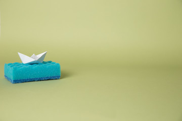 One blue sponge for washing dishes on a green background with an origami boat.