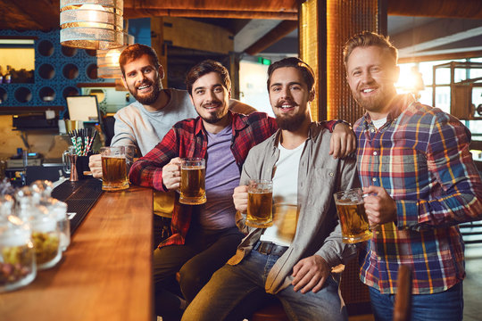 Friends With Glasses Of Beer Clinking While Standing At A Bar In A Bar Pub.