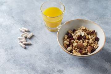 Bowl of granola with nuts,  cranberry, almonds and rasins. Sport supplements ( carnitine capsules ) in background. Bright stone  background. 
