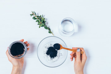 Female's hands add black charcoal powder to white cosmetic clay