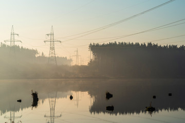 Obraz na płótnie Canvas Stumps of trees at dawn in the water against the background of a power line in the middle of the forest in the haze. Selective focus.