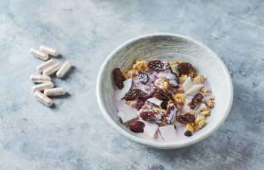 Bowl of granola with yogurt, nuts, cranberry and cocoanut. Sport supplements ( carnitine capsules ) in background. Bright stone  background.