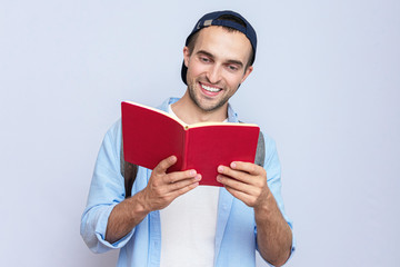 Happy student man with backpack reading a book, gray background
