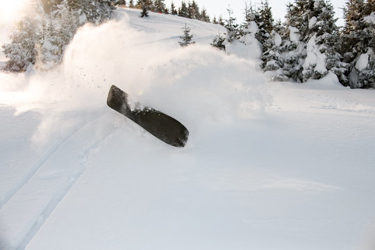 Snowboard falling in snow on a sunny day in mountains