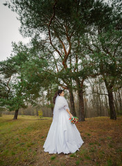Fototapeta na wymiar Happy bride in a beautiful wedding dress stands by the pine tree.