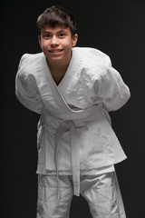 sport concept - a teenager dressed in martial arts clothing poses on a dark gray background, studio shoot