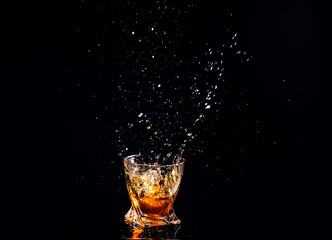Whiskey with splash on black background, brandy in a glass