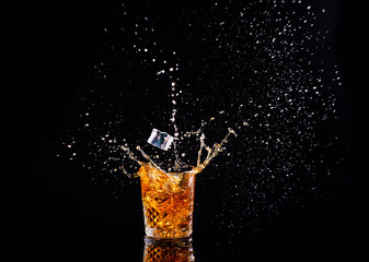 Whiskey with splash on black background, brandy in a glass