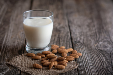 A glass with almond vegetable milk stands on a wooden table. Almond nuts are next to the glass.