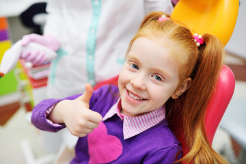 the child is a little red-haired girl smiling sitting in a dental chair.