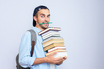 Nerd student with a stack of books and a pencil in his teeth, portrait, gray background, copy space