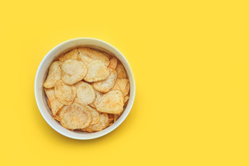 Crispy potato chips in bowl on yellow background, top view